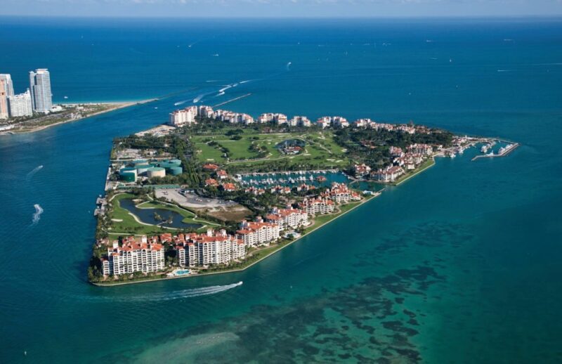 Aerial view of a densely developed island surrounded by turquoise waters, with high-rise buildings, green spaces, and luxury waterfront homes. Boats navigate the surrounding waters, enhancing the allure of luxury real estate branding.
