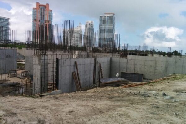 A construction site with concrete walls and exposed rebar, set against a backdrop of tall modern buildings under a cloudy sky. Amidst construction materials and debris, the scene hints at future luxury real estate branding opportunities.
