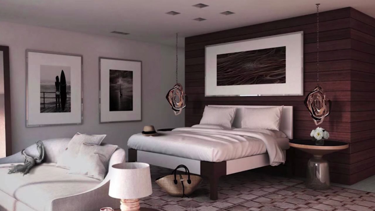 Modern bedroom with a large bed, white bedding, white sofa, and wall art. Wooden accent wall behind the bed, two hanging lights, a hat on the bench, and a woven basket on the floor.