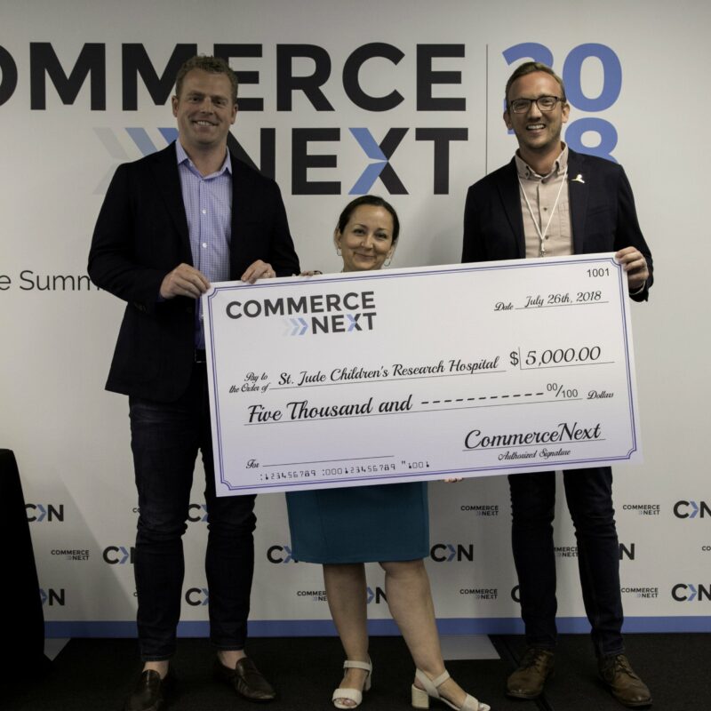 Three people holding a large check for $5,000 made out to St. Jude Children's Research Hospital. The event is CommerceNext 2018.