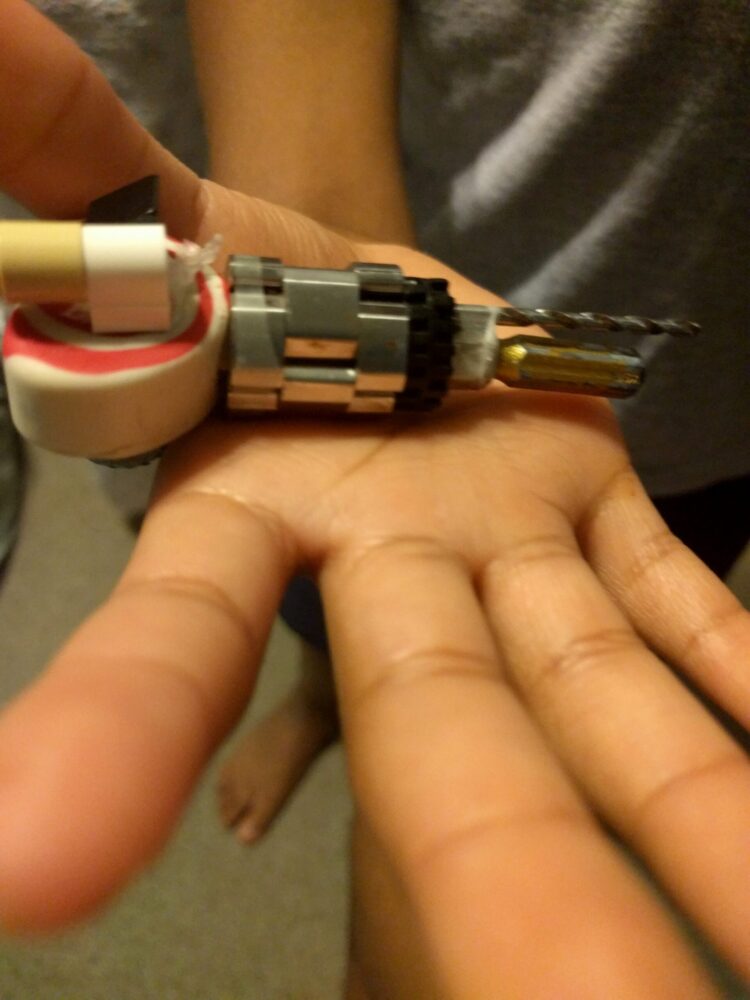 A hand holding a partially disassembled cylindrical device with exposed metal components and wiring, resembling the intricate inner workings of a mechanical pencil.