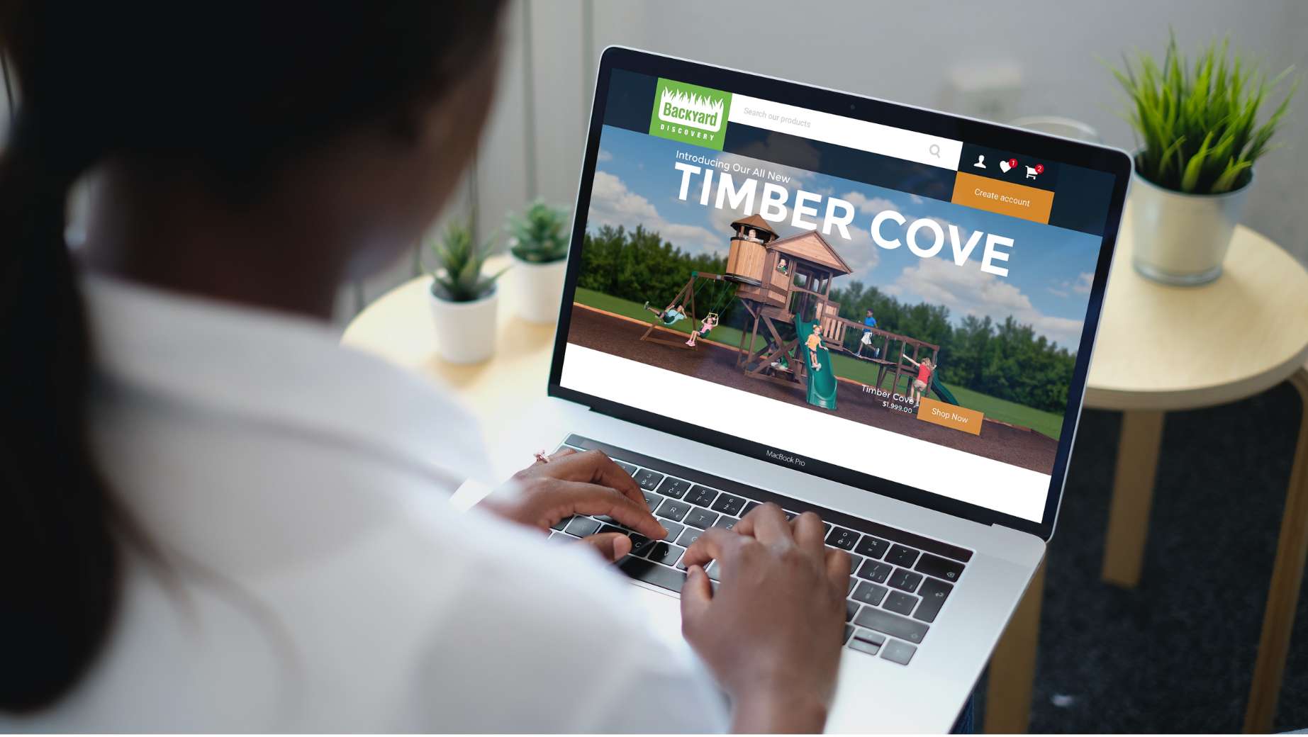 Person using a laptop displaying a website for "Timber Cove" with an image of a playground structure featuring the longest swing set.