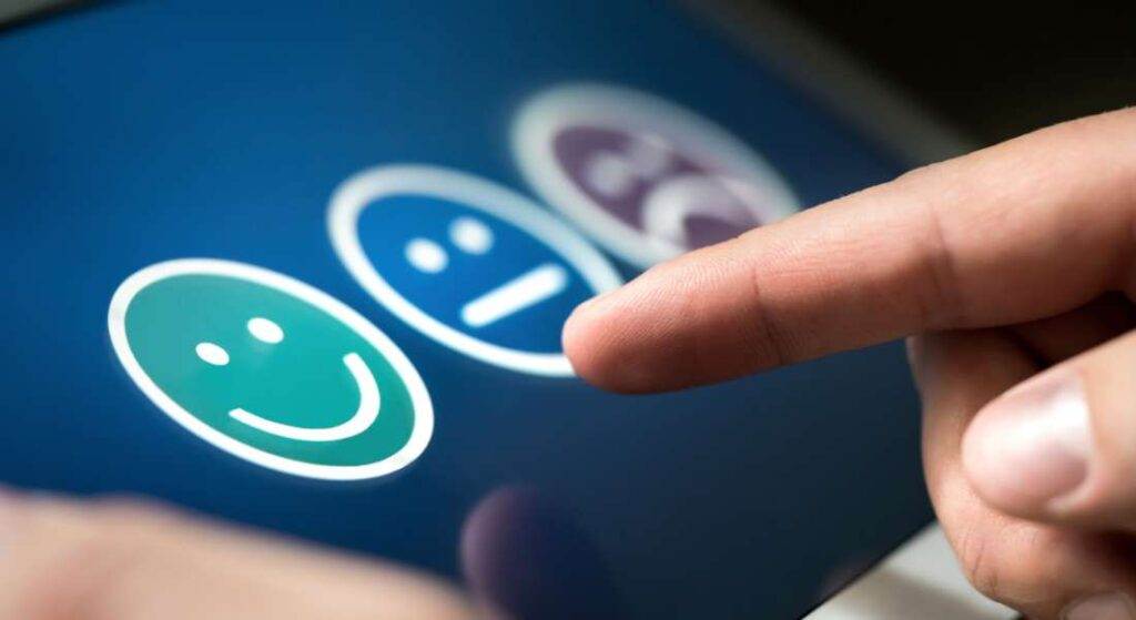 A person points to a touch screen displaying three emoticons: a happy face, a neutral face, and a sad face, highlighting the principles of user experience design.